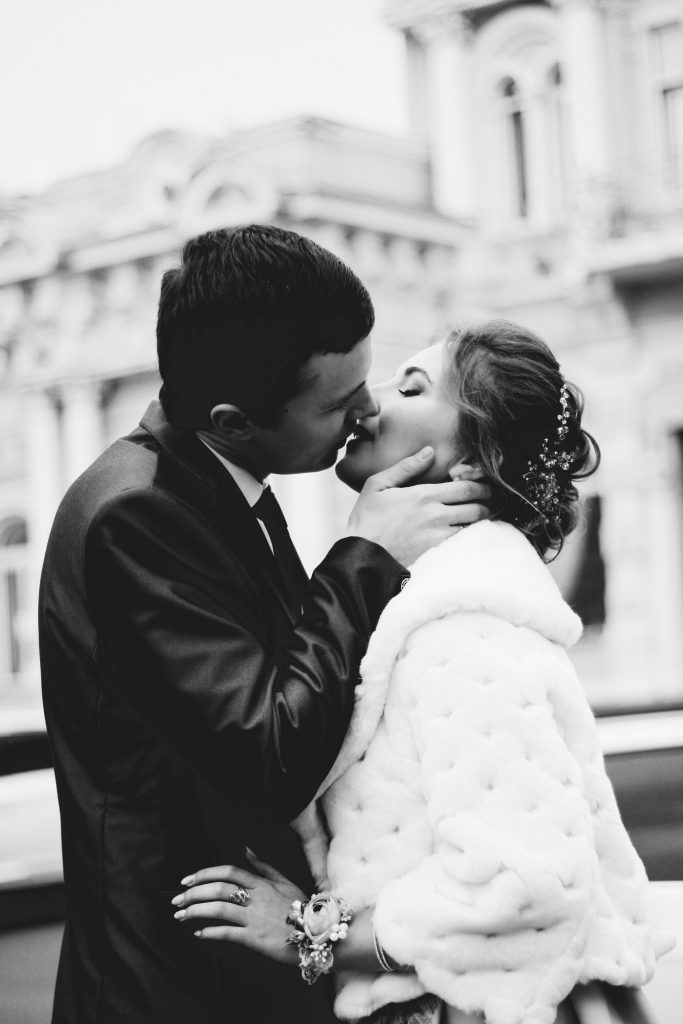 A black and white picture of a couple: bride and a groom kissing on their wedding day